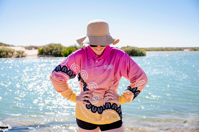Community Within Fishing Shirt - Woman smiling hands on hips by water, front portrait